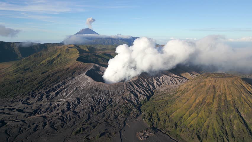 Aerial view of active Mount Bromo volcano emitting smoke with erupting Mount Semeru in the background. Stunning volcanic landscape in East Java, Indonesia. Raw nature, power, and geological beauty.