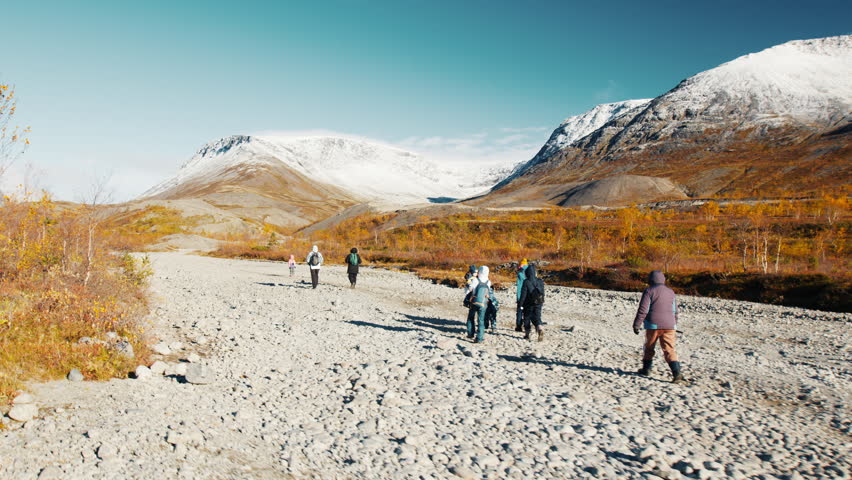 Group of hikers with kids walk on the autumn windy valley with stunning views. Hiking in the mountains. Khibiny Mountains, Russia