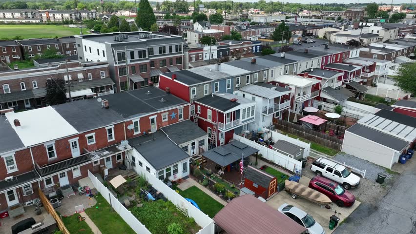 Aerial view of classic American row houses with flat roofs, brick facades and colorful siding. Back porches, fenced yards and rooftop details show historic urban architecture in neighborhood of USA.
