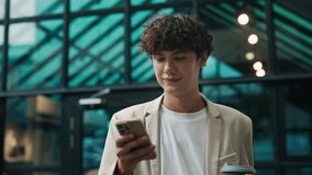 Portrait of happy businessman with coffee cup using smartphone against office building. Young man entrepreneur makes deals online via mobile app on street. Digital technology - Powered by Shutterstock - Get 15% off with code: PIKWIZARD15