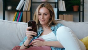 Video of beautiful young woman using her mobile phone sitting on couch at home - Powered by Shutterstock - Get 15% off with code: PIKWIZARD15