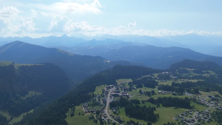 Aerial panorama revealing lac de peyre nestled among verdant slopes and rocky summits, sunlight illuminating alpine landscape