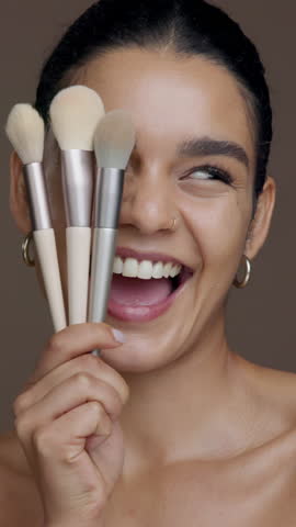 Brushes, makeup and face of woman in studio for grooming, foundation or facial glow with smile. Happy, cosmetic tools and portrait of female person from Mexico with cosmetology by brown background.