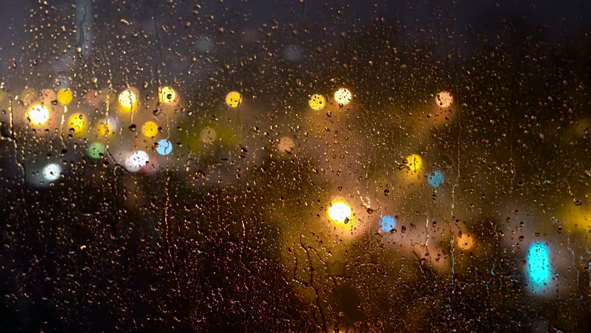 Blurred City Lights at Stormy Night with Lightnings Seen Through a Skyscraper Window with Rain Drops. Raindrops On Glass Window Against Night City Street During Thunderstorm. Melancholy Rain.