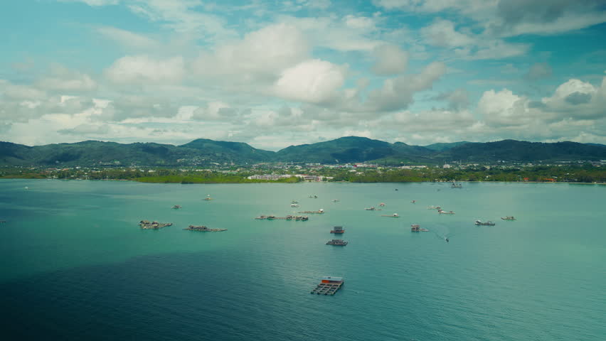 Aerial view of floating fish farms near Phuket, Thailand. Aquaculture structures in turquoise sea with mountains in background. Sustainable seafood production concept