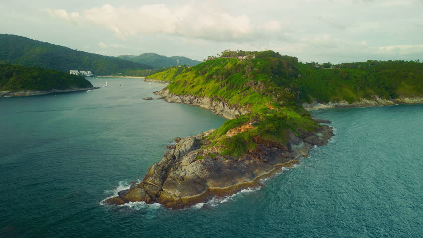 Scenic aerial view of Promthep Cape on Phuket Island, Thailand. Rugged rocky shoreline, lush green hills, and blue sea at sunset light. Iconic coastal landscape