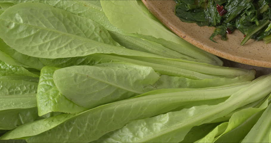 Fresh, young chicory leaves and a platter with Roman-style sautéed chicory greens (Cicoria Ripassata alla Romana) - an Italian tasty side dish. Table spin.