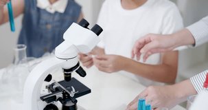 Closeup of Asian teacher guiding elementary school boy in adjusting microscope during primary science class with beakers and test tubes around as part of chemistry experiment in classroom lab - Powered by Shutterstock - Get 15% off with code: PIKWIZARD15