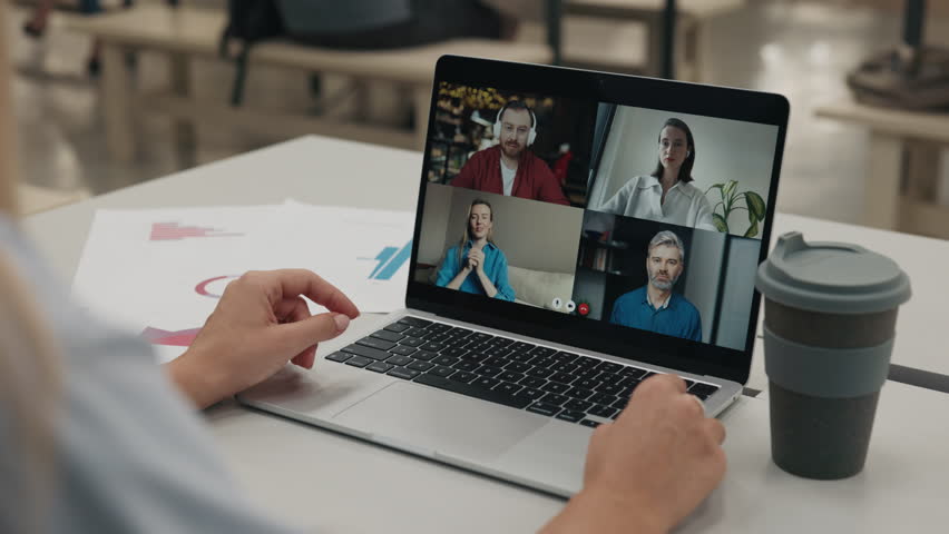 Woman participates in online zoom meeting with business colleagues via laptop in modern office setting. Manager engages in remote work fostering collaboration through technology