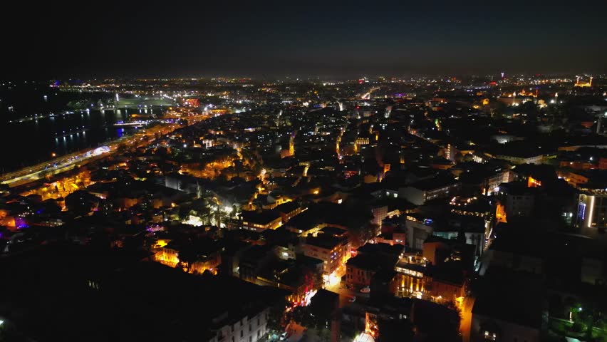 Wide night aerial of Istanbul showcasing streets filled with warm lights. The Bosphorus, roads and rooftops intertwine in a glowing network of Turkish urban life.