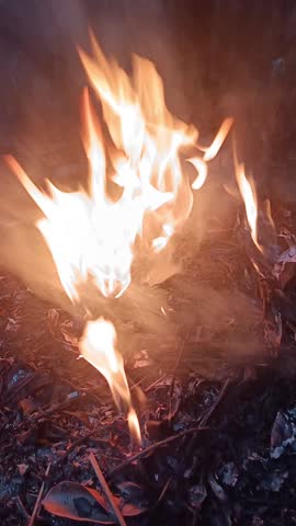 Intense flames and smoke rise from a burning pile of debris, illustrating open-air combustion or waste disposal, with a focus on the vivid orange and yellow hues of the fire.