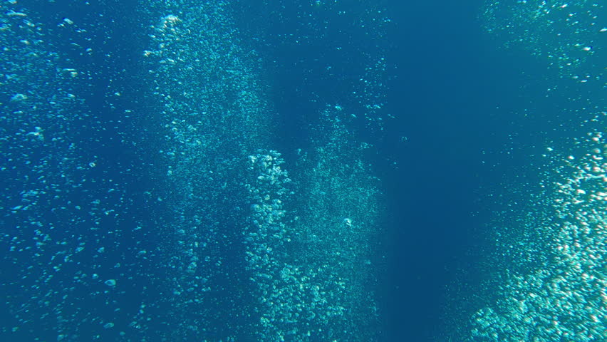 An endless stream of air bubbles rising upward from deep sea against blue water. Natural underwater background with air bubbles popping up from depths, concept of group scuba diving
