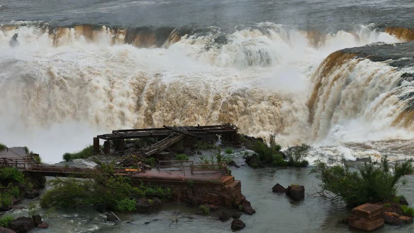 Aerial view of Iguazu Falls shows the river plunging between Argentina and Brazil. Heavy spray fills the air as water pours down the cliffs. Green jungle lines the edge of the famous landmark