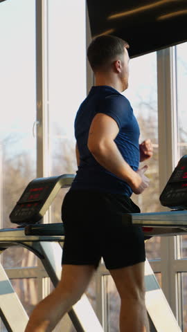 Man jogging on treadmill in sunny gym