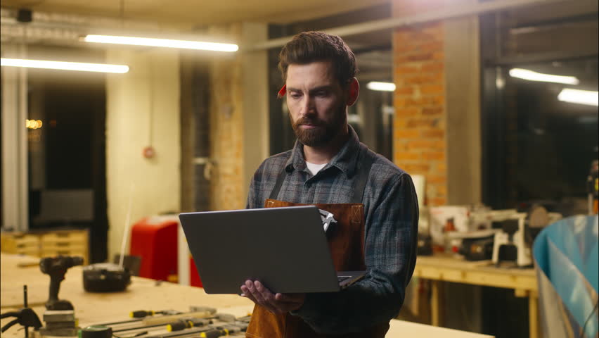 Positive Caucasian wood master man typing laptop online in workshop small business craftsman guy using computer device male joiner worker smile carpenter virtual shopping application Internet website