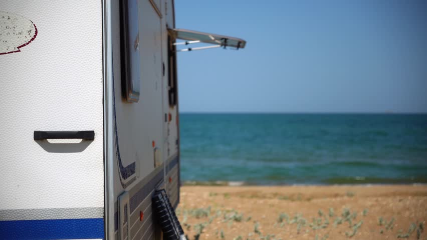 A trailer with an open window stands on the beach overlooking the sea, outside