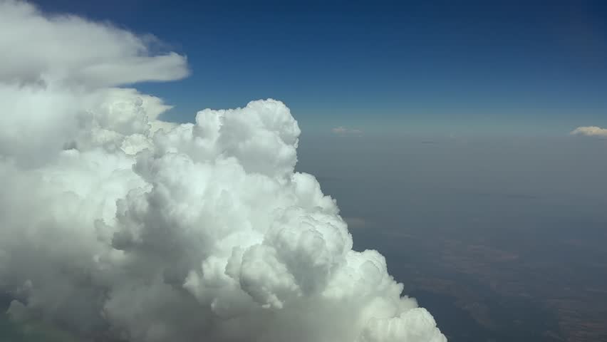 A pilot’s view in a real time flight close to the edge of a massive storm cumulonimbus cloud while flying at highaltitude at cruise, under a blue sky. Ultra-realistic 4K