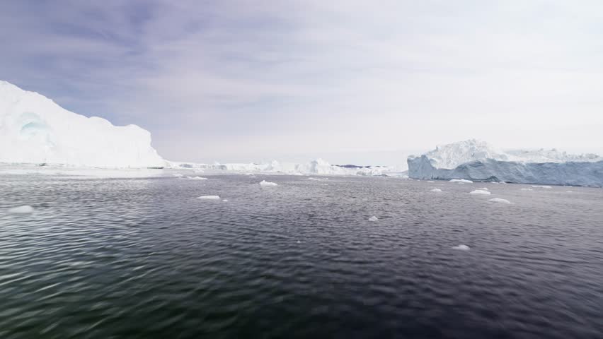 View from a boat gliding through the ice sea of the Disco Bay in Greenland, with big icebergs and chunks of ice surrounding the boat.