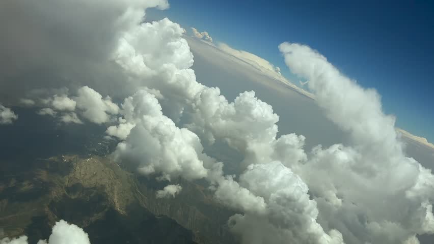 An aerial view taken from a jet cockpit while flying peacefully through some cottony cumulius clouds over a montainous landscape during a left turn. Ultra-realistic 4K shot.