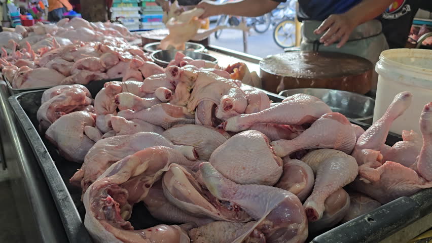 A wet market vendor chopping raw chicken meat with a cleaver on a round wooden board.