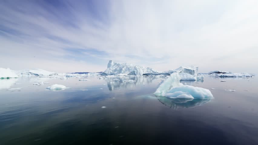 View from a boat gliding through the ice sea of the Disco Bay in Greenland, with big icebergs and chunks of ice surrounding the boat.