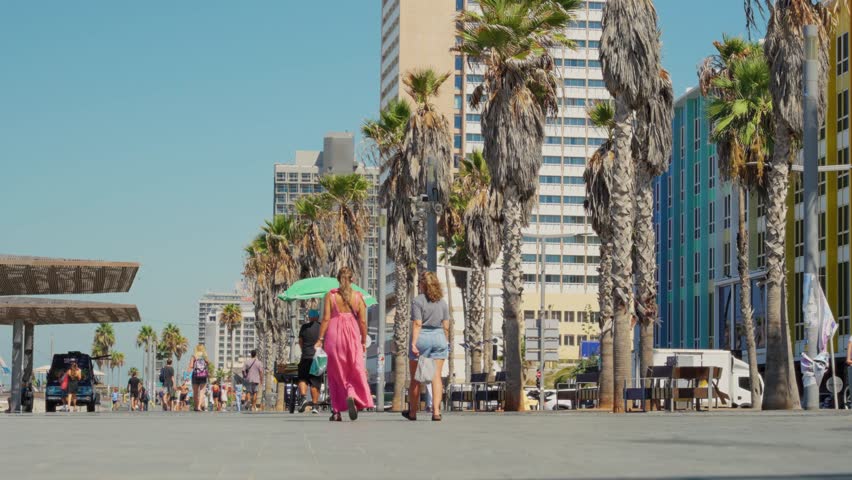 Tourists and locals walking on boardwalk or promenade in Tel Aviv beach. People strolling and sightseeing or going to swim in Mediterranean Sea in Israel during hot summer vacation outdoors