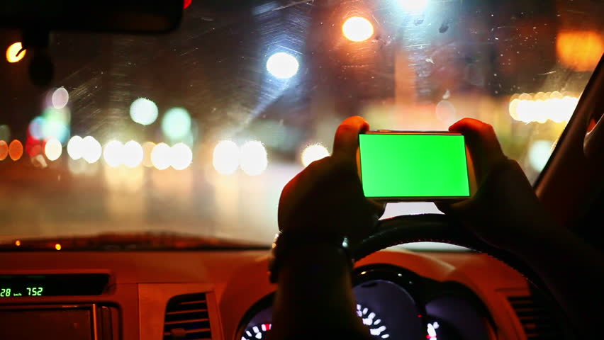 Safely Parked to Use the Phone.
holding a phone with a green screen while using a fingertip to scroll. Surrounded by the soft glow of streetlights and distant cars, the blurred night lights