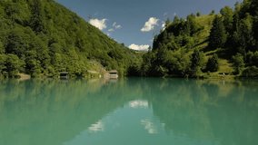 A low drone view of Klammsee Lake that reflects the surrounding green, forested mountains and a clear, blue sky with scattered clouds in Austria - Powered by Shutterstock - Get 15% off with code: PIKWIZARD15