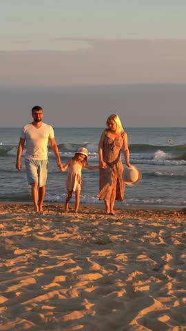 Happy family with child walks on sand beach at sea at sunset. Summer vacation travel holiday. People outdoors by water. Vertical shot