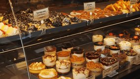Assorted pastries and desserts including labeled fruit tartelettes and chocolate treats in a glass display case at a bakery in Athens, Greece. Mousse, tiramisu, custards in glasses. No people - Powered by Shutterstock - Get 15% off with code: PIKWIZARD15