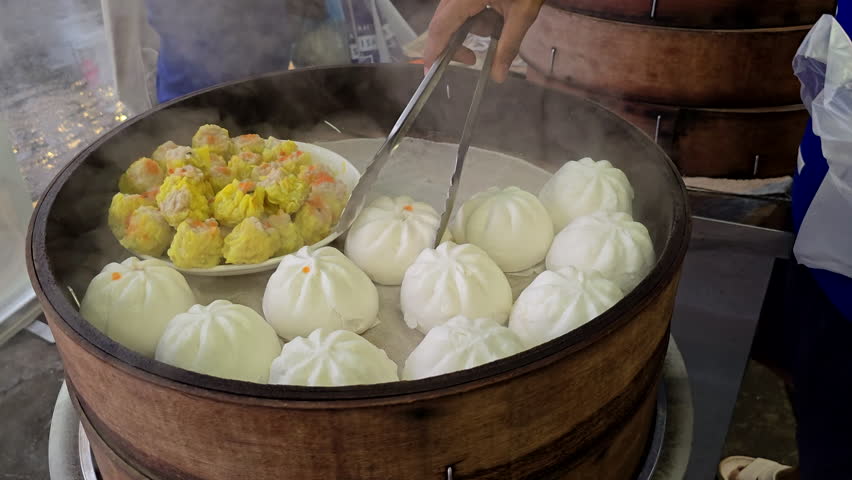 Close-up view of freshly steamed buns and siu mai being served from a large bamboo steamer at a local dim sum stall.