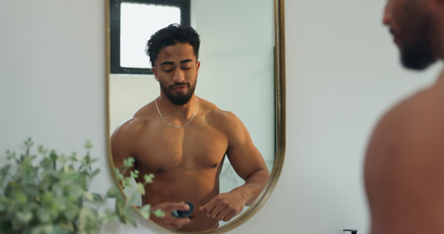 Happy man, deodorant and spraying with mirror for hygiene, odor or masculine fragrance in bathroom. Shirtless, male person or armpit with smile or perfume for underarm scent or fresh smell in home