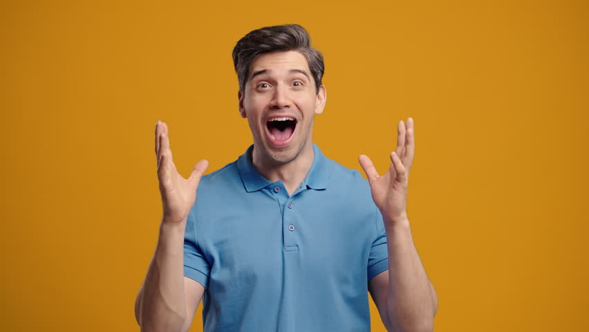 Surprised handsome man making mind blown gesture on warm yellow background