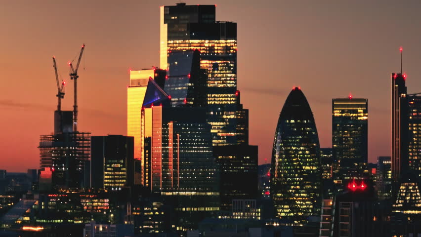 Warm sunset over London iconic skyline, featuring 30 St Mary Axe (The Gherkin), with construction cranes symbolizing growth in the bustling metropolis. Cityscape night background. Drone flight footage