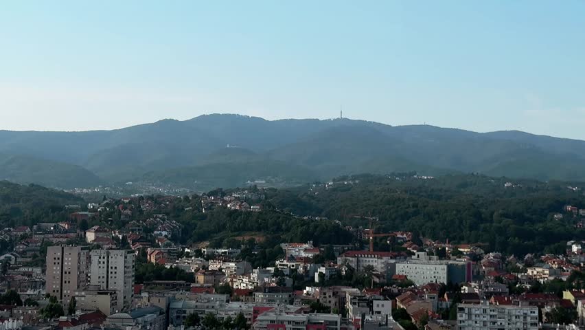 Cityscape video panorama of Zagreb, Croatia, city with Medvednica Mountain in summer day in top view. Landscape footage with skyscrapers, buildings, hill horizon with TV tower in aerial viewpoint.