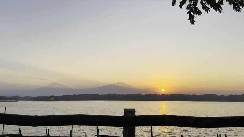 A stunning sunset view over Cengklik Reservoir in Boyolali, Central Java, Indonesia. The warm golden light of the setting sun reflects gently on the calm water surface.