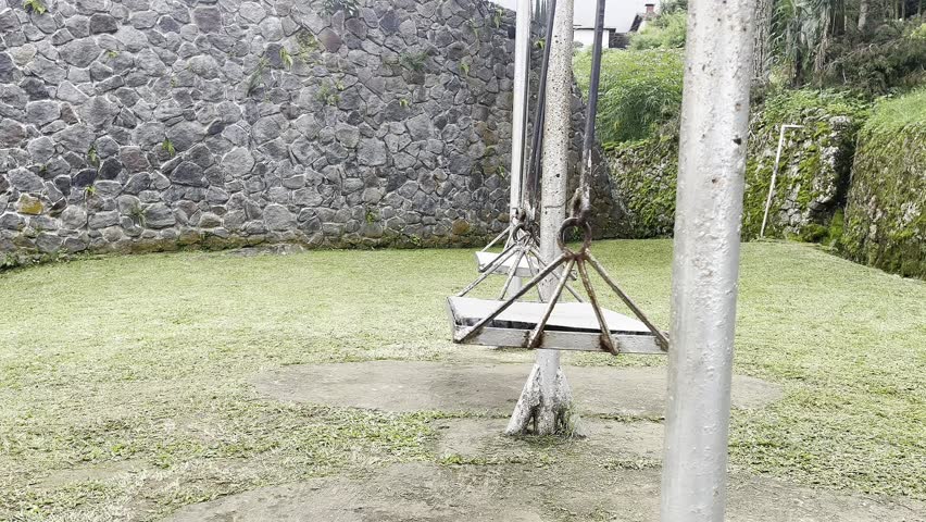 An old metal swing in a grassy yard surrounded by a stone wall. The swing