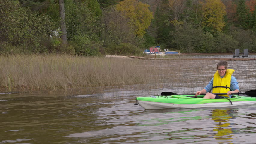Young woman kayaking near shore with reflected beauty of reeds and water