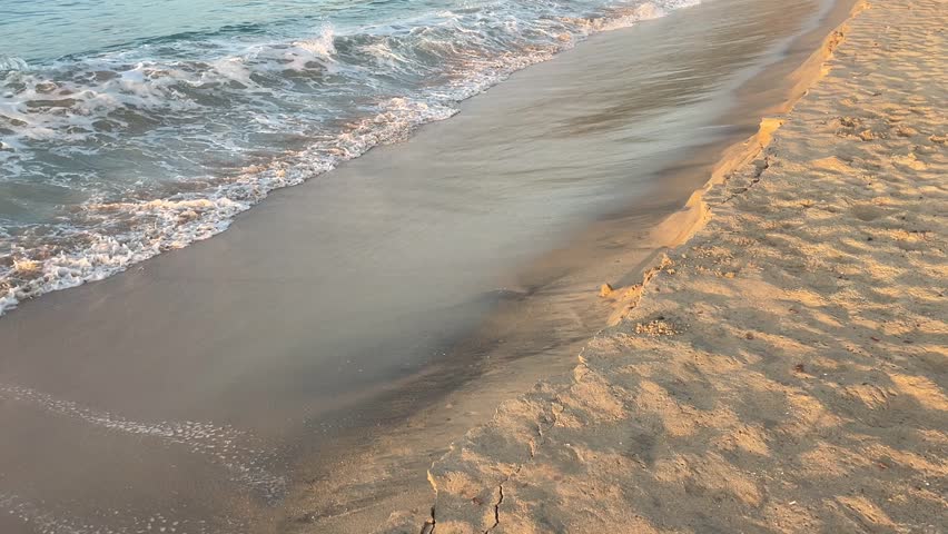 Rhythmic motion of gentle waves washing ashore on a sandy beach. The foamy white crests beautifully contrast with the smooth, wet sand, creating a serene and timeless scene.