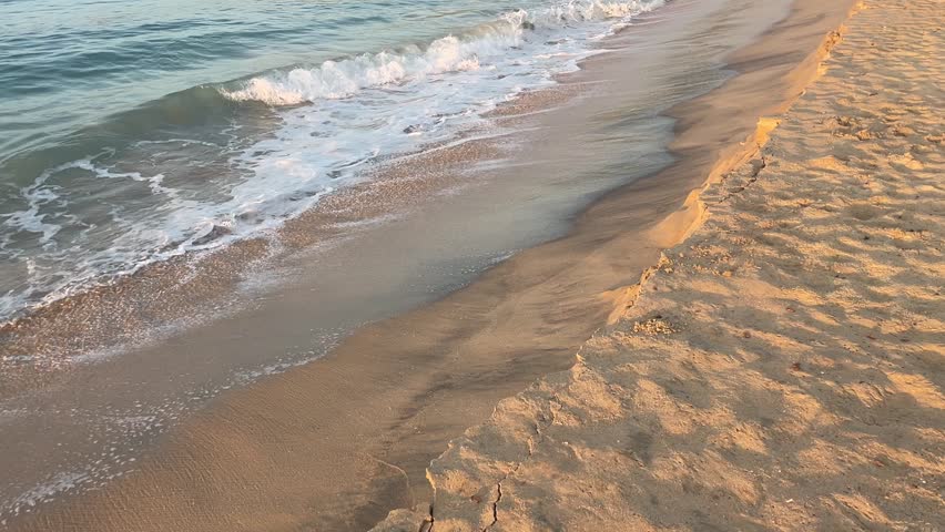 Rhythmic motion of gentle waves washing ashore on a sandy beach. The foamy white crests beautifully contrast with the smooth, wet sand, creating a serene and timeless scene.