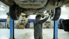 Mechanic performing detailed vehicle inspection underneath car, using flashlight while checking mechanical system on raised hydraulic lift in professional automotive workshop - Powered by Shutterstock - Get 15% off with code: PIKWIZARD15