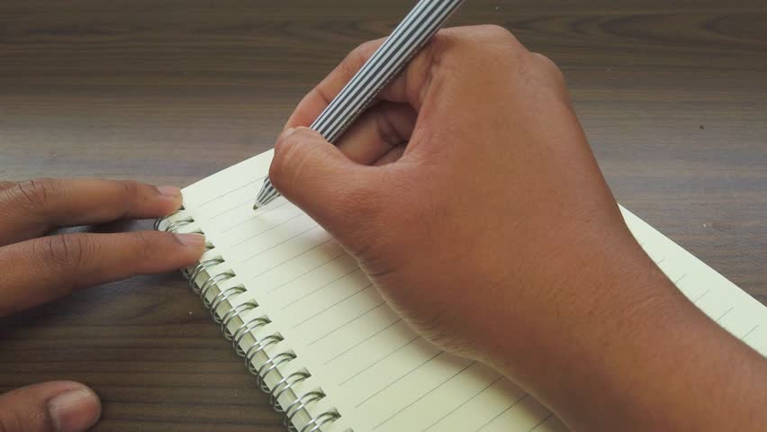 Hand of Asian man writing April title on the notebook.