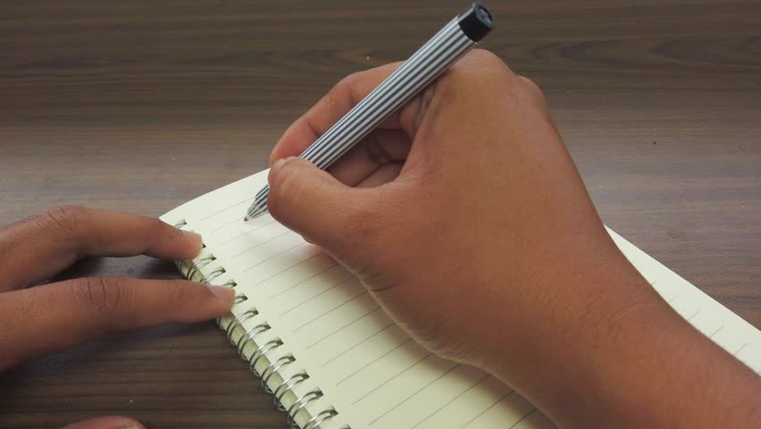 hand of Asian man writing December title on the notebook.