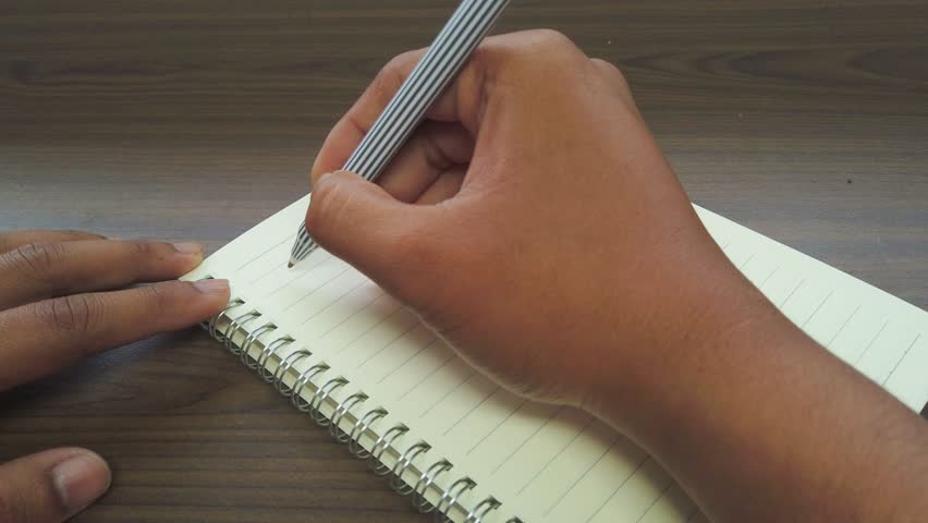 Hand of Asian man writing February title on the notebook.