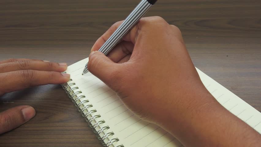 Hand of asian man writing January title on the notebook.