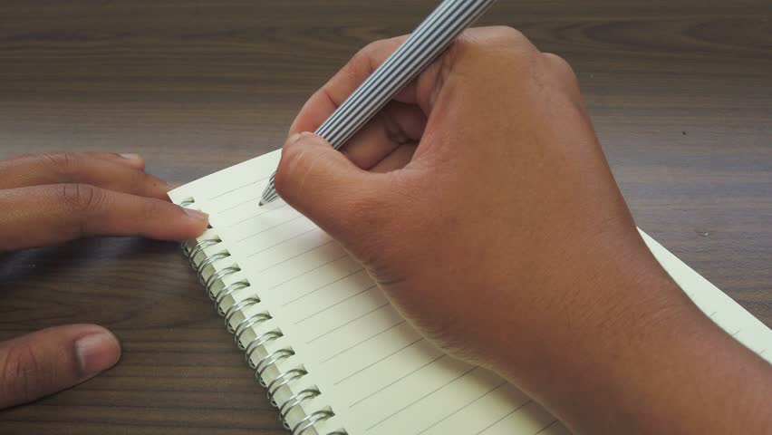 Hand of Asian man writing July title on the notebook.