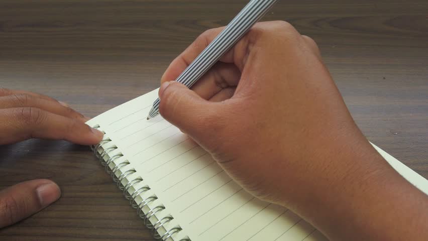 Hand on Asian man writing June title on the notebook.