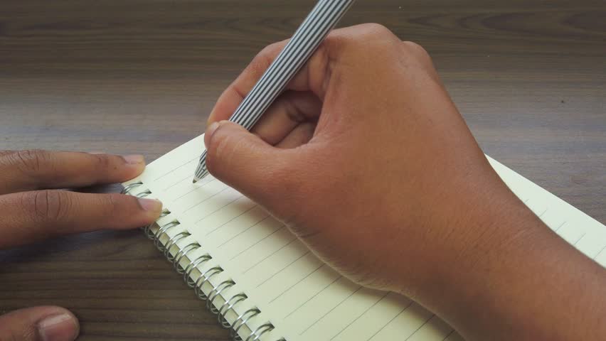 Hand of Asian man writing Marcg title on the notebook.