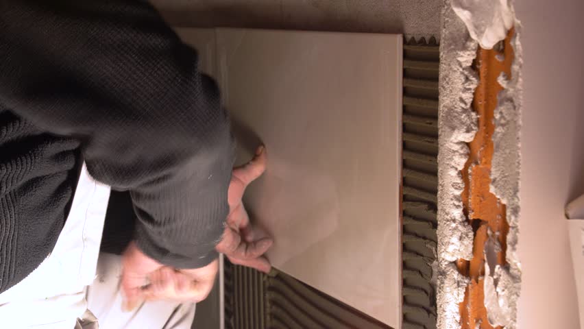 Worker carefully pressing tile onto adhesive during bathroom wall installation work