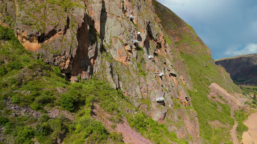 A breathtaking aerial approach reveals the Skylodge Adventure Suites' transparent glass pods dramatically suspended on a cliffside 1,300 feet above Peru's Sacred Valley.